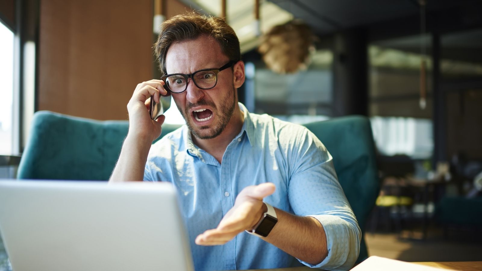 angry businessman yelling at his computer while talking on the phone