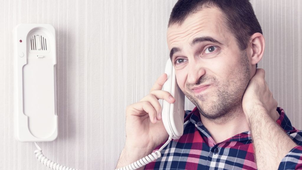 frustrated man talking on a land line phone connected to the wall