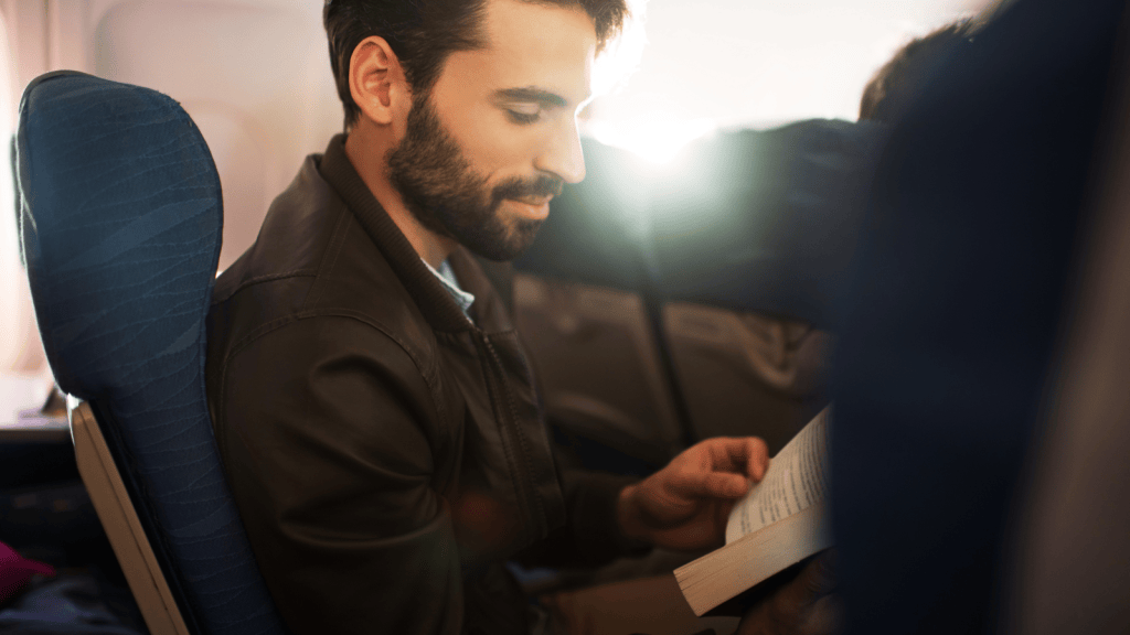 He Was Forced into Middle Seats on 14 Hour Flights—Until He Uncovered a Fleet Class Fare Upgrade Loophole man sitting in an airplane reading a book