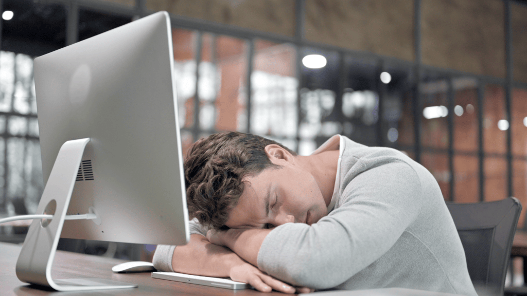 One Worker Has Found A Hotel Job Where He Barely Has To Work, And He’s Completely Comfortable Collecting A Full Week’s Pay tired man taking a nap at the reception desk