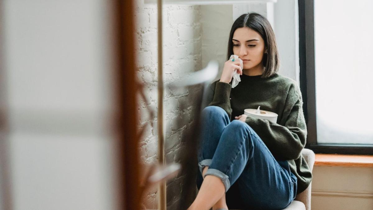 Woman Said Yes To A Friendly Roommate Who Kept Borrowing Her Clothes For Months, So She Was Left With A Loose Skirt, A Cluttered Bed, And A Guilty Conscience After Finally Saying No upset woman in green sweater sitting on couch